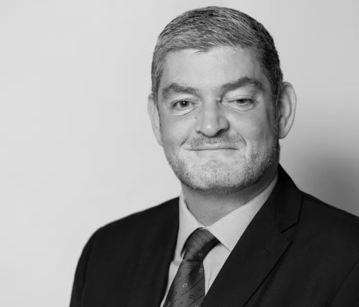 A man in a suit and tie poses against a plain background in a black and white portrait.